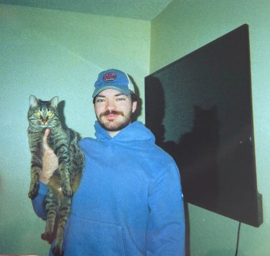 A film photo of Jack in a blue hoodie holding up a tabby cat