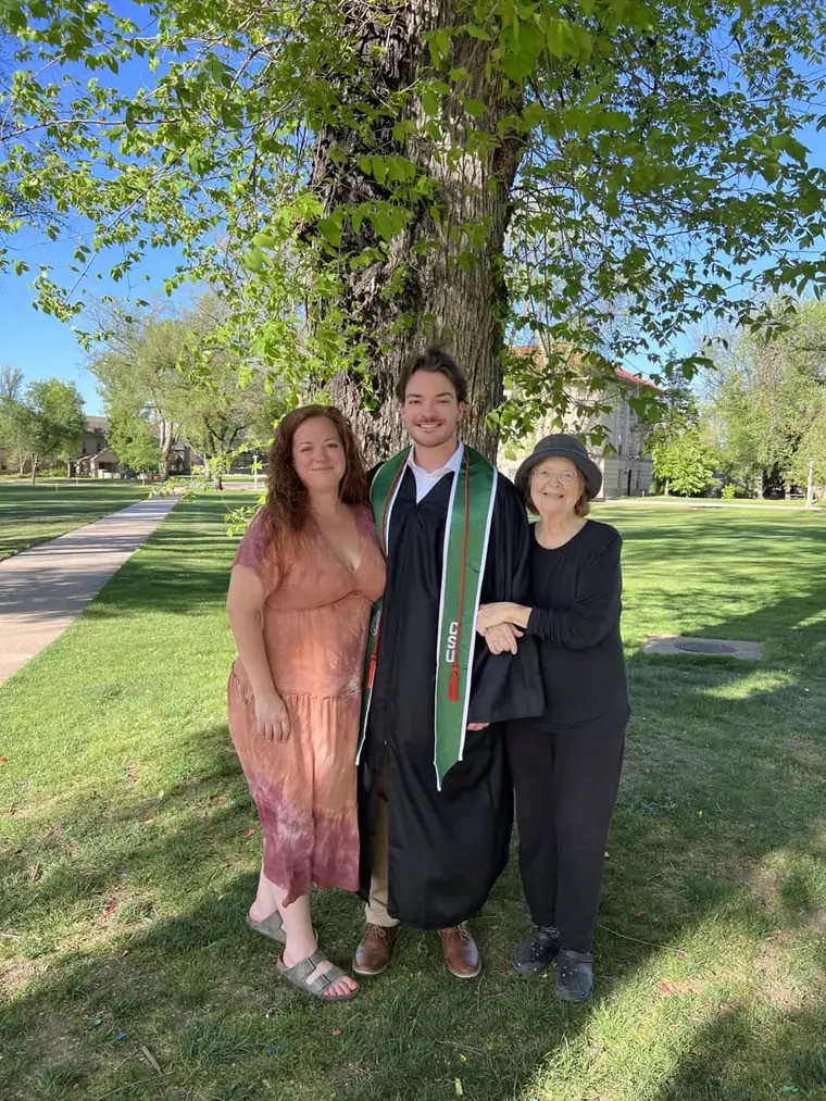 Jack in a graduation gown with two others on a campus lawn