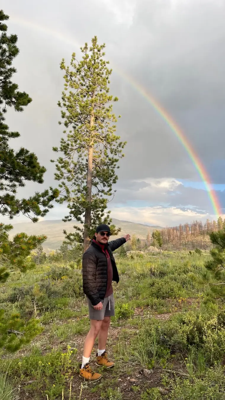 Jack pointing at a rainbow over a pine-covered hillside